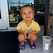 Brooklyn joined the competition — help win amazing prizes! toddler, child, smiling, yellow_shirt, purple_crocs, squatting, concrete, porch, plastic_cup, water, glass_door, reflection, person, outdoor, sunlight, short_hair, casual_clothing, happy, cute, daytime