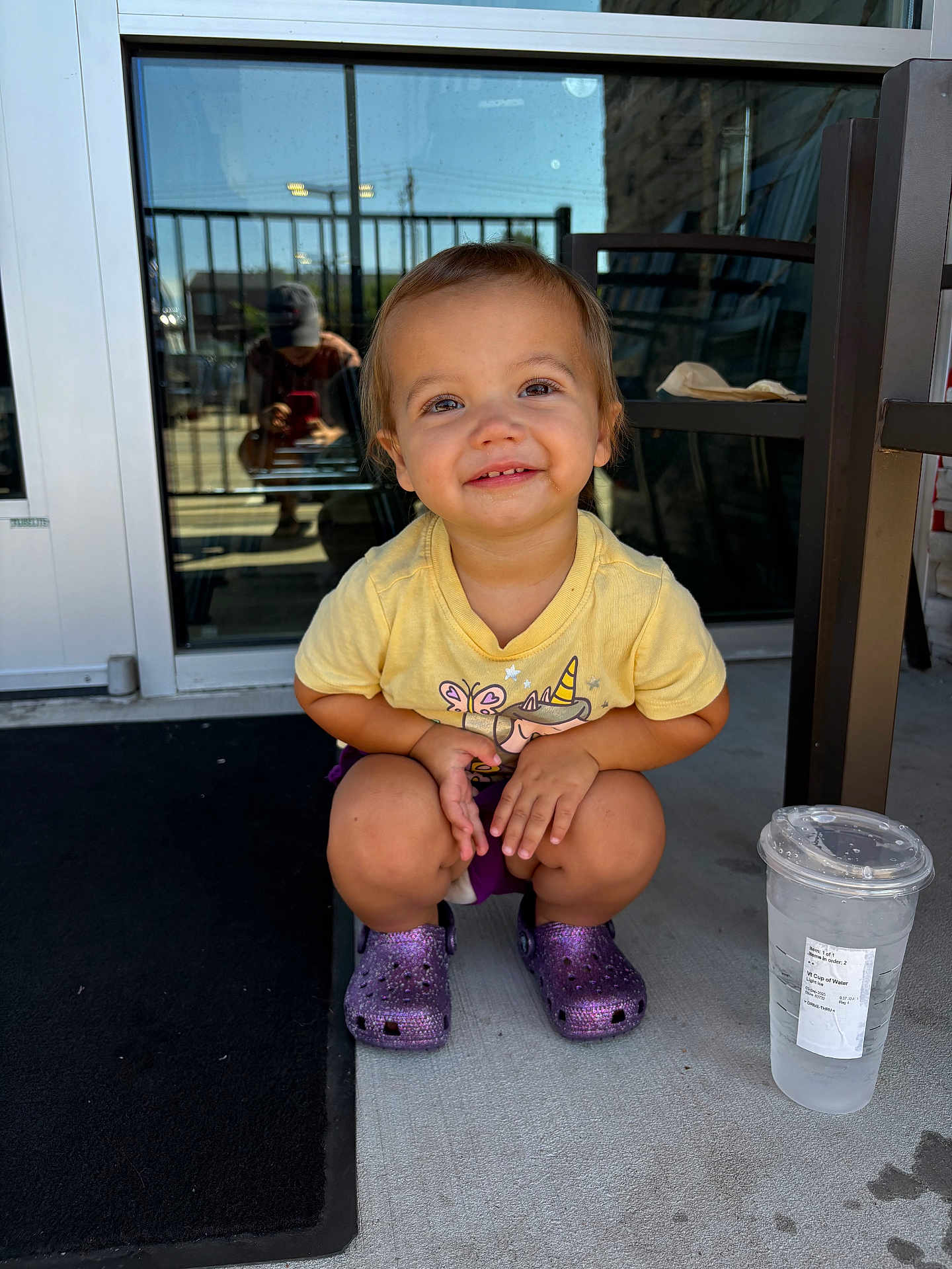 Brooklyn joined the competition — help win amazing prizes! toddler, child, smiling, yellow_shirt, purple_crocs, squatting, concrete, porch, plastic_cup, water, glass_door, reflection, person, outdoor, sunlight, short_hair, casual_clothing, happy, cute, daytime