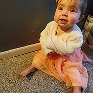 Evelynn is registered to the contest to win money with this photo: baby, carpet, child, cozy, cute, dress, expression, floor, foot, hair_bow, indoor, infant, jacket, looking_up, person, sitting, smiling, soft_clothing, wall, young_child