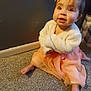 baby, carpet, child, cozy, cute, dress, expression, floor, foot, hair_bow, indoor, infant, jacket, looking_up, person, sitting, smiling, soft_clothing, wall, young_child
