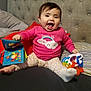 Evelynn joined the competition — help win amazing prizes! baby, bed, cheerful, child, clouds, cute, feet, happy, headboard, indoors, laughing, patterned_pants, person, pillow, pink_sweater, playful, rainbow, sitting, smiling, toy