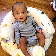 Luca is registered to the contest to win money with this photo: baby, infant, bottle, blue_clothing, baby_seat, animal_pattern, wooden_floor, sitting, indoors, cute, child, smiling, happy, face, head, person, foot, hand, bottle_cap, eyes