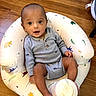 baby, infant, bottle, blue_clothing, baby_seat, animal_pattern, wooden_floor, sitting, indoors, cute, child, smiling, happy, face, head, person, foot, hand, bottle_cap, eyes