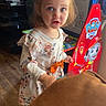 Leilani joined the competition — help win amazing prizes! child, toddler, indoor, pigtails, curious, toy, paw_patrol, arcade_game, wooden_floor, casual_clothing, floral_dress, person, home_interior, furniture, brown_couch, light, face, expression, playful, standing