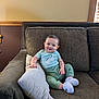 baby, smiling, couch, pillow, indoor, child, infant, clothing, socks, happy, face, person, furniture, home, wood, window, cozy, seated, cute, relaxed