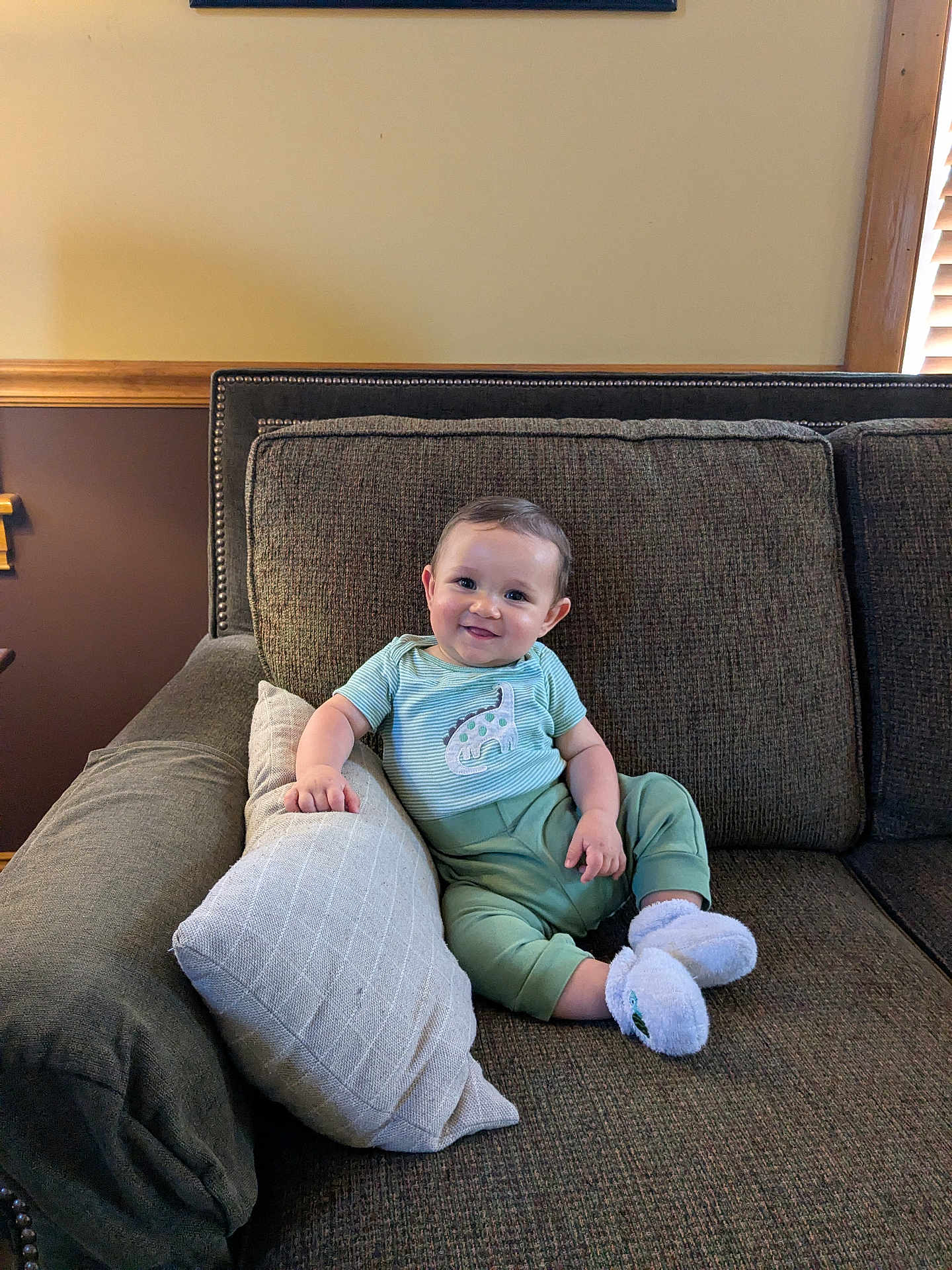 Leland is registered to the contest to win money with this photo: baby, smiling, couch, pillow, indoor, child, infant, clothing, socks, happy, face, person, furniture, home, wood, window, cozy, seated, cute, relaxed