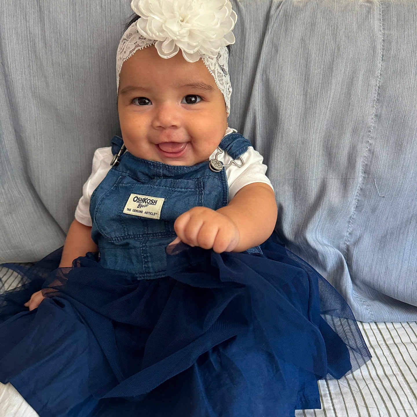 Isa is registered to the contest to win money with this photo: baby, bonnet, cap, clothing, couch, dress, face, formalwear, furniture, glove, happy, hat, head, jeans, pants, person, photography, portrait, sitting, smile