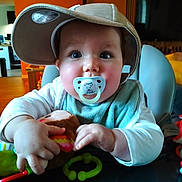 Soën a rejoint le concours — aidez-le/la à gagner de superbes lots ! baby, bib, big_eyes, cap, cheeks, chubby_hands, closeup, cute, furniture, hands, hat, highchair, indoor, infant, living_room, pacifier, stuffed_toy, table, television, toy