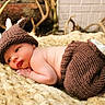 baby, infant, knit_hat, knit_pants, antlers, blanket, lying_down, face, skin, newborn, cute, soft_texture, indoors, warm_colors, portrait, baby_clothing, resting, cozy, headwear, decor
