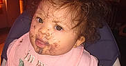 Eliana is registered to the contest to win money with this photo: baby, messy, food_stains, bib, high_chair, curly_hair, face, child, indoor, pink_clothing, expression, hand, portrait, cute, toddler, person, seat, feeding, curious, mess