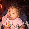 baby, messy, food_stains, bib, high_chair, curly_hair, face, child, indoor, pink_clothing, expression, hand, portrait, cute, toddler, person, seat, feeding, curious, mess