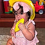 toddler, child, yellow_helmet, pink_dress, bow, toy, plastic_toy, carpet, indoor, play, cute, baby, sitting, curious, wooden_shelf, background, colorful, hand, face, person
