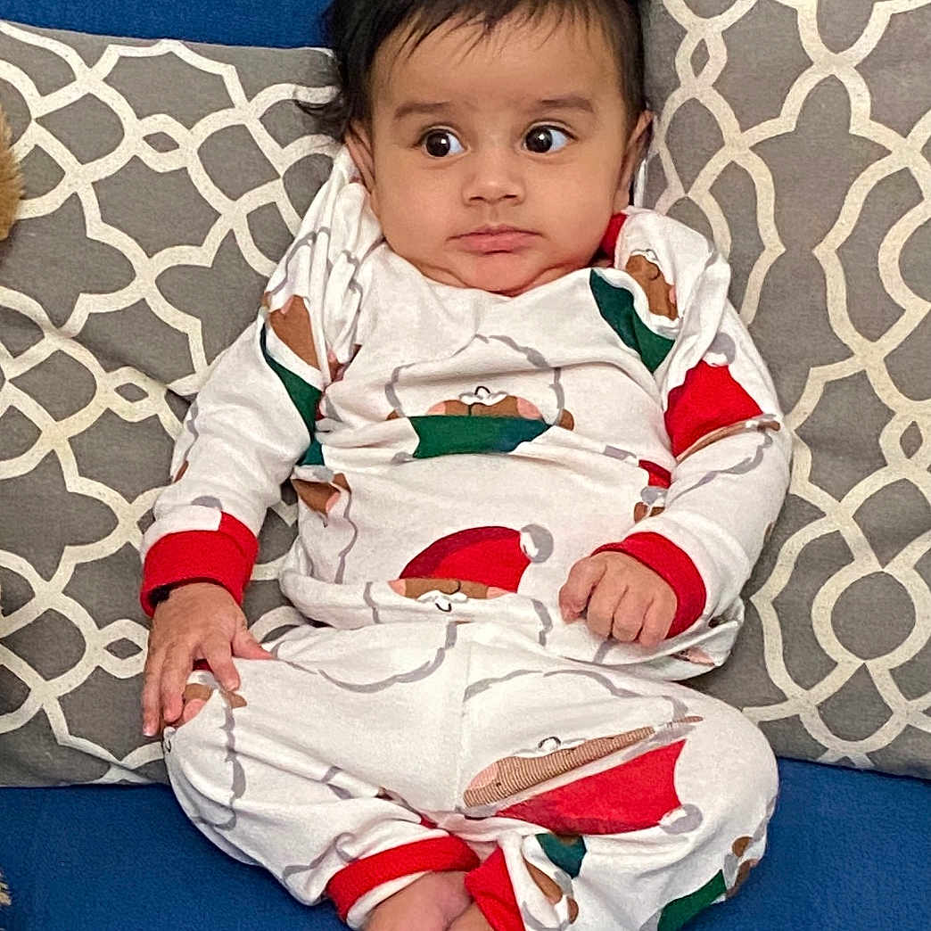 Prayan is registered to the contest to win money with this photo: baby, bodypart, clothing, couch, cushion, dress, face, finger, furniture, hand, head, homedecor, indoors, pajamas, pants, person, photography, pillow, portrait, sitting
