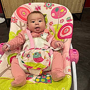 Yüna a rejoint le concours — aidez-le/la à gagner de superbes lots ! baby, child, pink_outfit, baby_rocker, colorful, bird_pattern, flower_pattern, indoor, cute, face, tongue_out, seat, straps, floor, cabinet, wooden_cabinet, playful, infant, happy, person