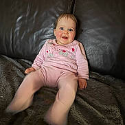 Victoria a rejoint le concours — aidez-le/la à gagner de superbes lots ! baby, child, smiling, pink_clothing, teddy_bear_design, blue_eyes, drool, leather_couch, blanket, indoor, happy, sitting, portrait, young_child, cozy, furniture, person, cute, motion_blur, rosy_cheeks