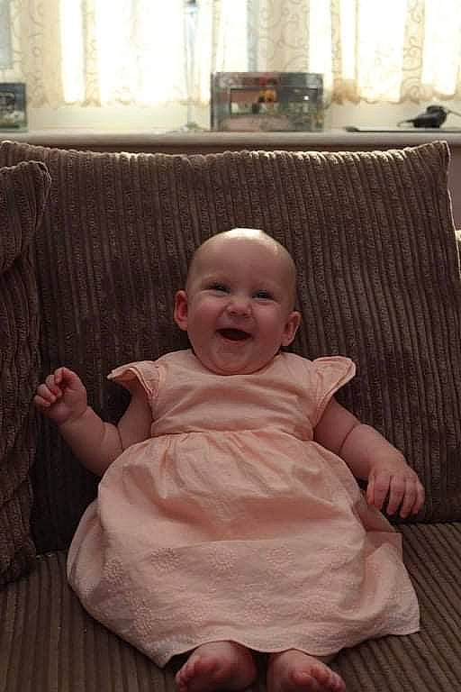 Poppy joined the competition — help win amazing prizes! baby, baby_toddler_clothing, cheek, comfort, couch, dress, event, finger, flooring, fun, happy, hardwood, lap, living_room, person, room, sitting, skin, smile, toddler