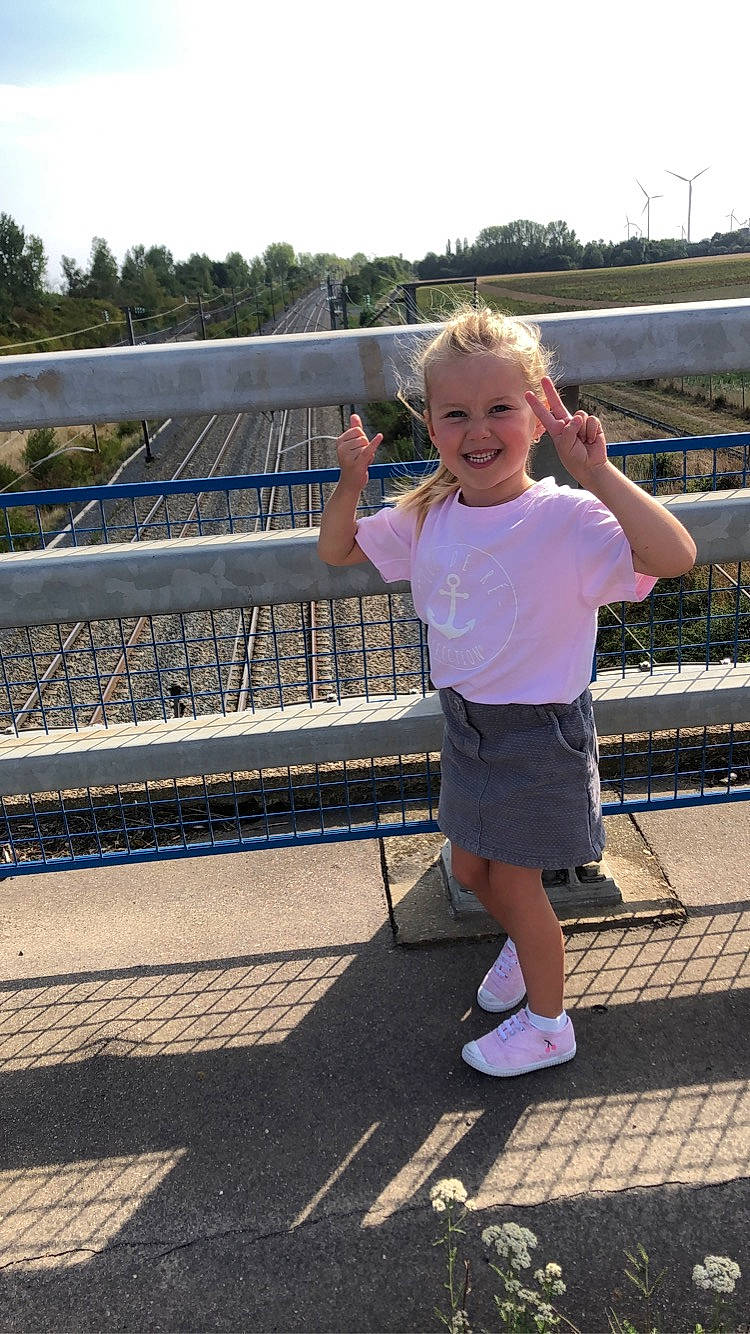 Joy participe au concours pour gagner de l'argent avec cette photo : baby_toddler_clothing, child, city, electric_blue, fence, fun, happy, joy, leisure, magenta, person, recreation, sky, smile, standing, t_shirt, toddler, travel, tree