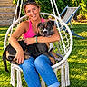 backyard, blue_jeans, bracelet, companion, dog, garden, greenery, hanging_chair, lawn, outdoor, pet, pink_shirt, portrait, relaxed, smiling, summer, sunglasses, sunlight, tattoo, woman