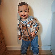 Noé participe au concours pour gagner de l'argent avec cette photo : child, toddler, smiling, standing, plaid_shirt, jeans, sneakers, indoor, hardwood_floor, wall, shadow, portrait, happy, face, eyes, hair, shoes, hood, buttoned_shirt, wooden_drawer