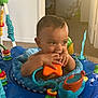 baby, infant, child, toy, activity_center, orange_star, blue, indoor, carpet, play, hands, chewing, face, smile, curious, seat, colorful, plastic, young, cute
