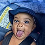 baby, child, face, hat, tongue, car_seat, seatbelt, warning_label, closeup, expression, playful, cute, infant, headwear, strap, person, skin, indoors, young, smile