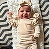 baby, blanket, cheerful, clothing, cozy, face, hand, hat, headband, indoor, infant, leg, lying_down, onesie, pillow, plush, portrait, smile, soft_texture, zigzag_pattern