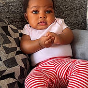 Giovanna is registered to the contest to win money with this photo: baby, infant, child, cute, pink_shirt, striped_pants, couch, pillow, pattern, indoor, portrait, hands, face, eyes, expression, seated, young, adorable, clothing, home