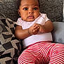 baby, infant, child, cute, pink_shirt, striped_pants, couch, pillow, pattern, indoor, portrait, hands, face, eyes, expression, seated, young, adorable, clothing, home