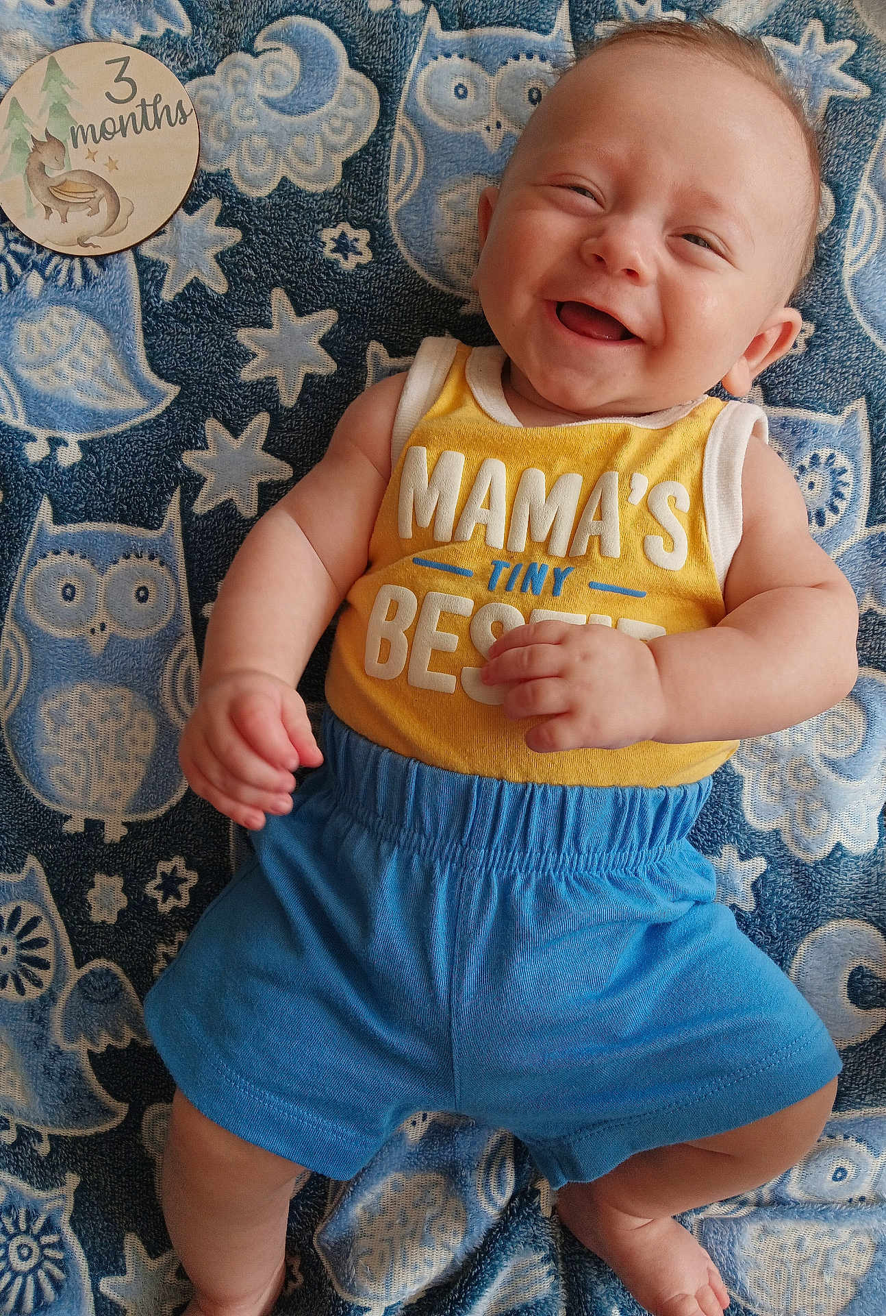 Matthias joined the competition — help win amazing prizes! baby, smiling, infant, yellow_tank_top, blue_shorts, owl_pattern, blanket, milestone_card, 3_months, happy, cute, child, lying_down, portrait, indoor, soft_texture, baby_clothes, hand, foot, face