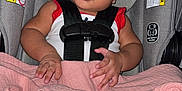 Cimani is registered to the contest to win money with this photo: baby, car_seat, blanket, headband, infant, child, straps, seat, pink, gray, curly_hair, portrait, indoors, clothing, person, cute, hands, face, young, sitting