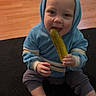 baby, blue_clothing, carpet, casual, child, cute, eating, floor, happy, home, hoodie, indoor, infant, person, pickle, playful, sitting, smiling, socks, wooden_floor