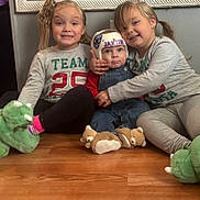 Jaxsin joined the competition — help win amazing prizes! animal_slippers, baby, casual_clothing, child, cozy, family, floor, gray_wall, happy, helmet, hugging, indoor, long_hair, overalls, pigtails, sitting, slippers, smiling, toddler, wooden_floor