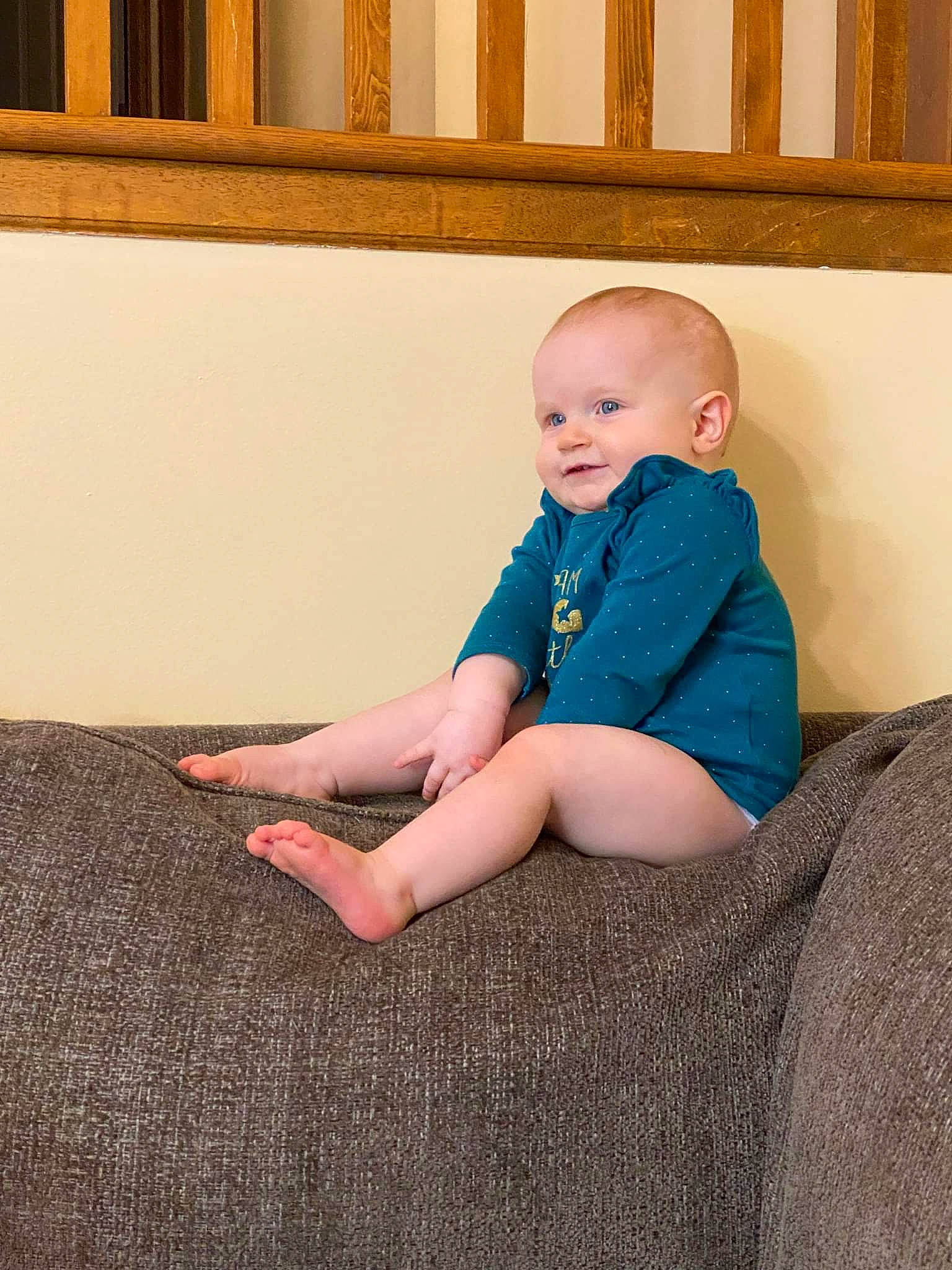 Mae is registered to the contest to win money with this photo: baby, baby_toddler_clothing, barefoot, child, comfort, facial_expression, finger, floor, flooring, hardwood, human_leg, knee, person, sitting, skin, sleeve, smile, standing, t_shirt, toddler