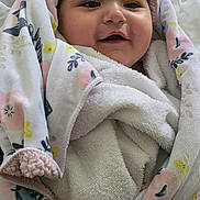 Heaven joined the competition — help win amazing prizes! baby, smiling, blanket, towel, hand, red_nails, floral_pattern, wrapped, cozy, cute, infant, portrait, indoors, soft_texture, happy, child, person, fabric, bed, comfort