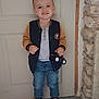 Leo a rejoint le concours — aidez-le/la à gagner de superbes lots ! toddler, child, smile, toy, tractor, jacket, jeans, sneakers, door, indoor, stone_wall, happy, cute, standing, person, clothing, footwear, portrait, casual, playful