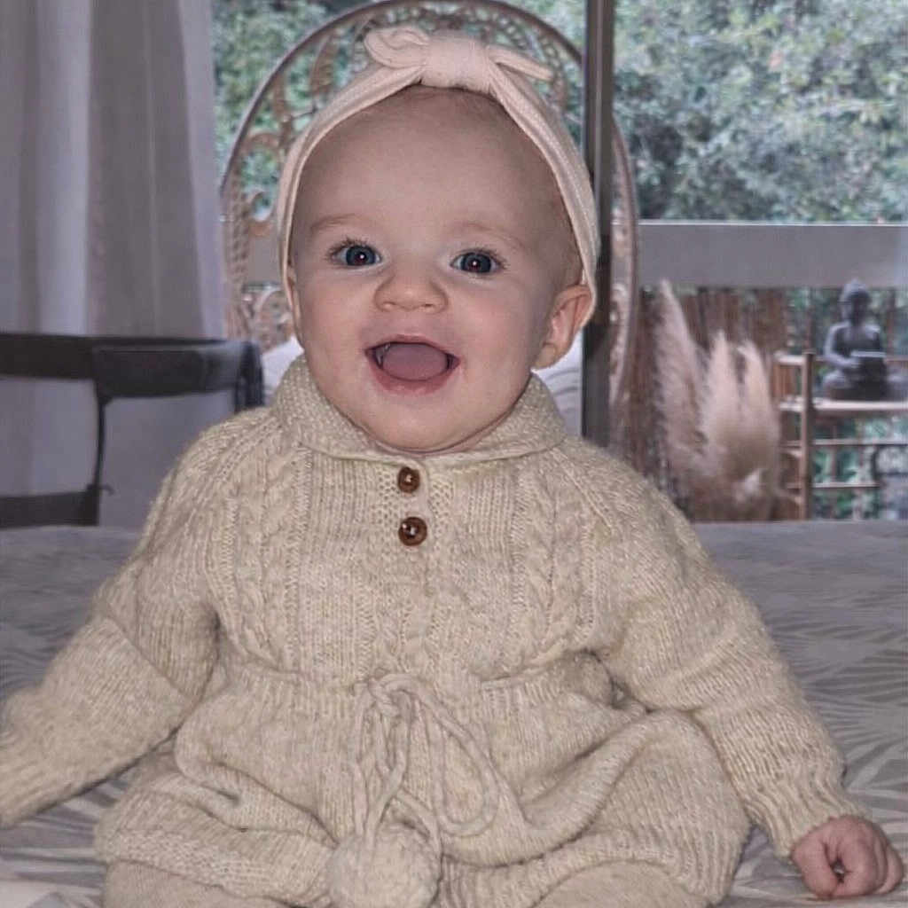 June participe au concours pour gagner de l'argent avec cette photo : baby, bed, child, clothing, cozy, cute, face, happy, headband, indoor, infant, knitwear, person, portrait, room, sitting, smiling, toddler, warm, window