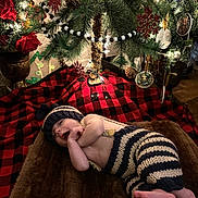 Tyrus joined the competition — help win amazing prizes! baby, infant, christmas_tree, ornaments, blanket, knit_clothing, hat, striped_pants, decorations, lights, plaid, groot_ornament, pine_cones, red_rose, toddler, holiday, festive, indoor, smiling, cute