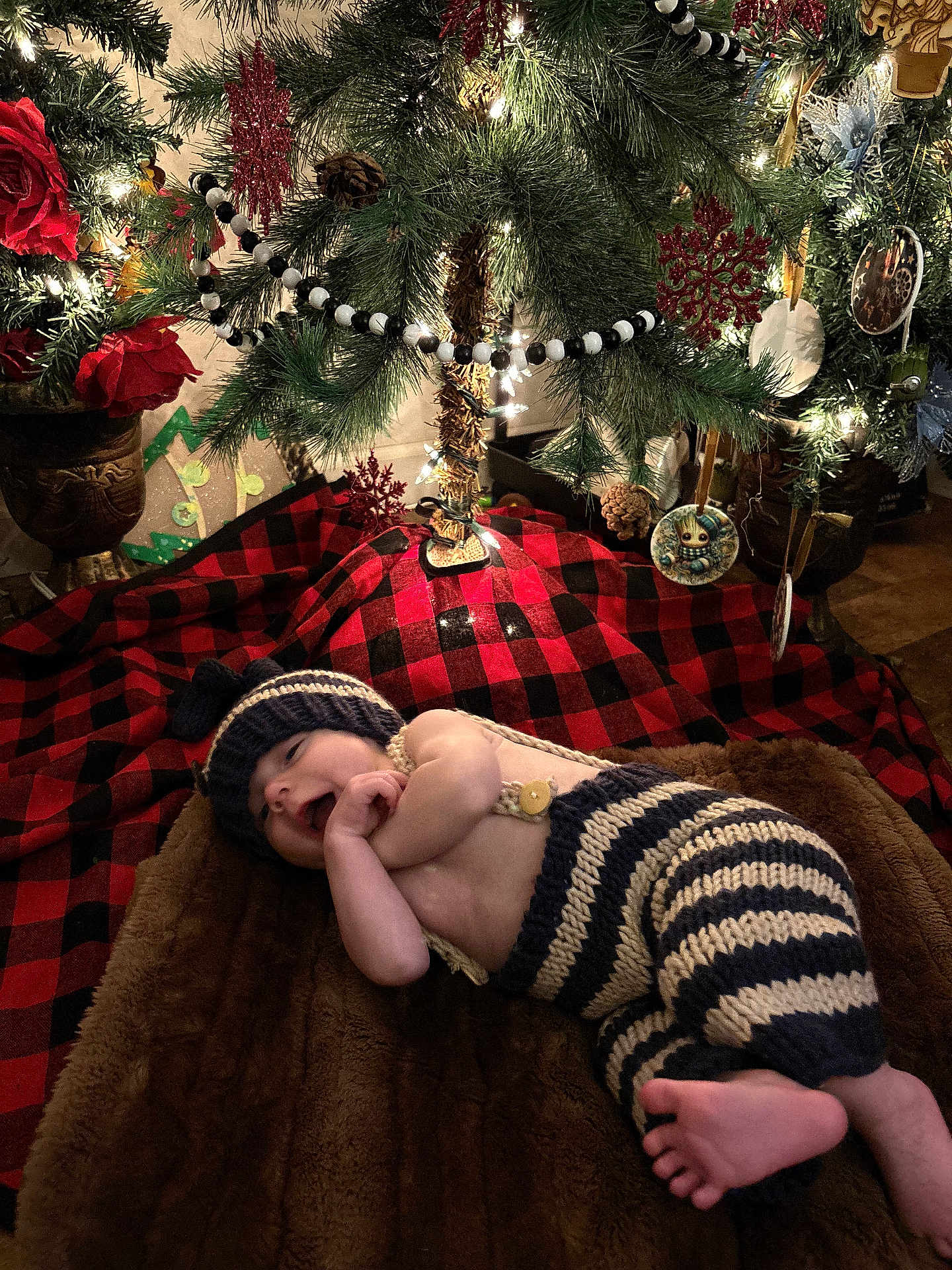 Tyrus joined the competition — help win amazing prizes! baby, infant, christmas_tree, ornaments, blanket, knit_clothing, hat, striped_pants, decorations, lights, plaid, groot_ornament, pine_cones, red_rose, toddler, holiday, festive, indoor, smiling, cute