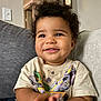 toddler, child, smiling, curly_hair, indoor, couch, tshirt, dinosaur, toy, happy, person, young_child, portrait, seated, casual_clothing, living_room, cute, playful, baby, home