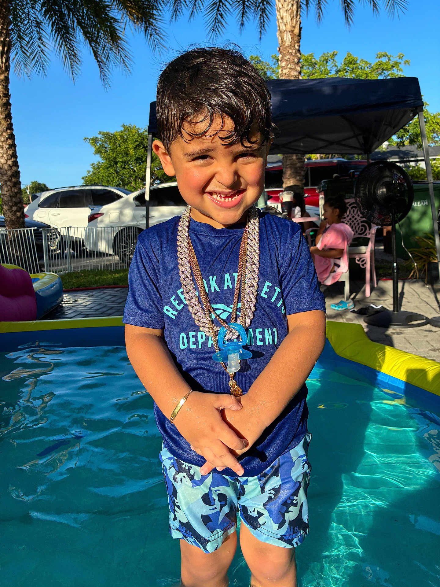 Cyphyr Pineda joined the competition — help win amazing prizes! child, boy, pool, water, swimwear, chains, pacifier, smile, outdoor, sunlight, summer, palm_tree, vacation, happy, playing, blue_shirt, shorts, bracelet, tent, background_people