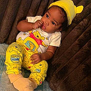 Zahmir joined the competition — help win amazing prizes! baby, child, infant, portrait, smiling, sitting, lying_down, yellow_hat, animal_hat, pajamas, winnie_the_pooh, cartoon, blanket, couch, plush, indoor, cozy, face, hand, sock