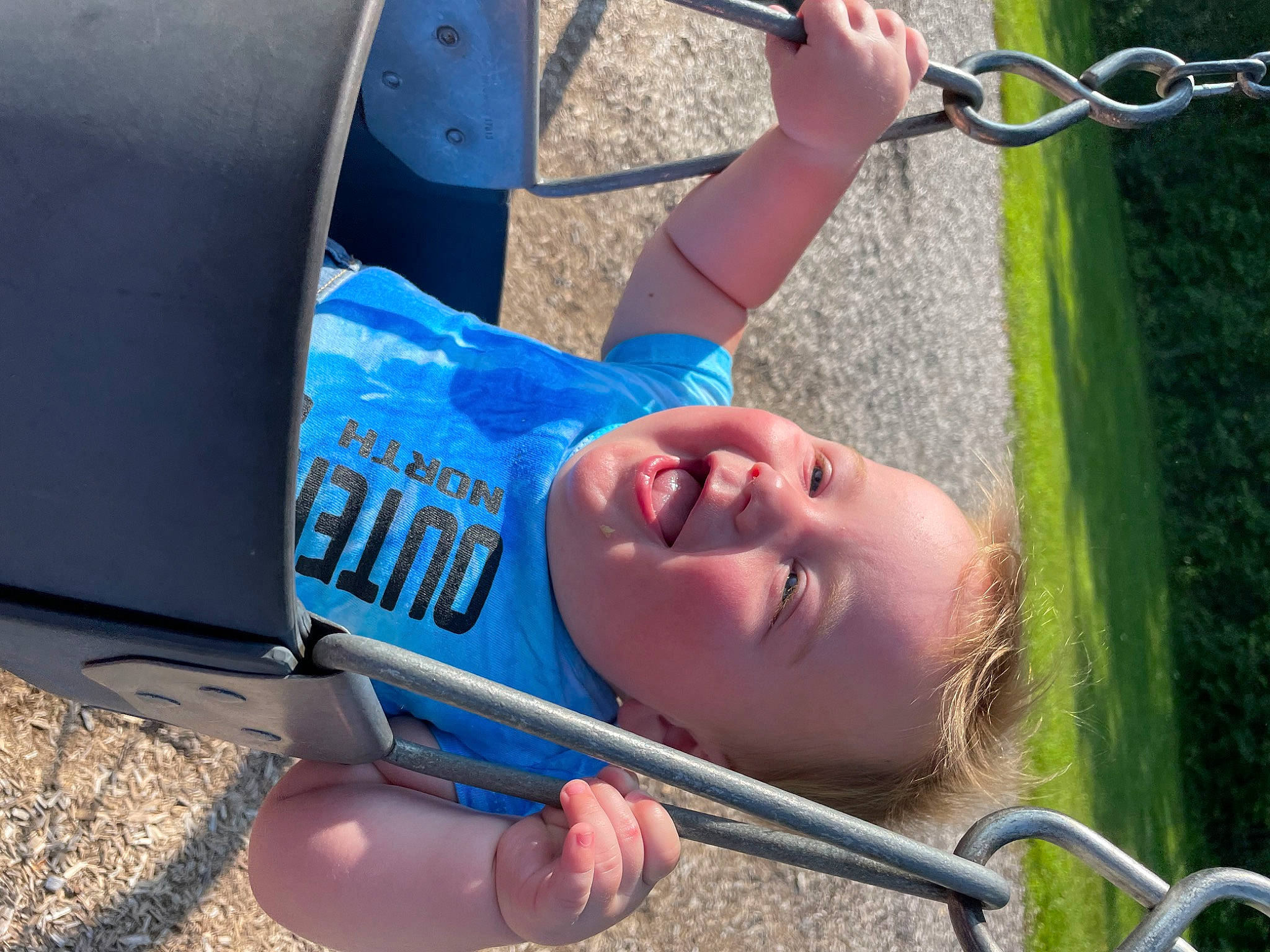 Colter is registered to the contest to win money with this photo: automotive_tire, bumper, child, cool, elbow, electric_blue, fun, grass, green, happy, leisure, outdoor_play_equipment, person, play, recreation, smile, snapshot, swing, toddler, tree