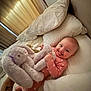 baby, bed, pillow, plush_toy, bunny, onesie, smiling, infant, blanket, furniture, indoor, curtains, soft_toy, child, cute, happy, person, cozy, sleepwear, nursery