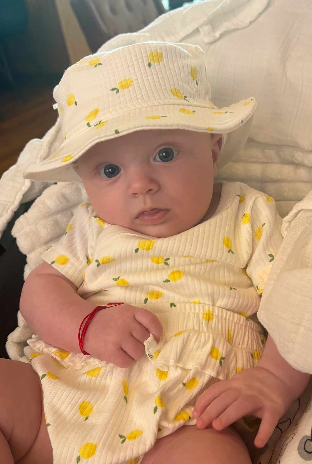 Cassandra is registered to the contest to win money with this photo: baby, infant, hat, clothing, yellow, lemon_pattern, cute, child, portrait, hand, face, eyes, indoors, soft_lighting, cozy, fabric, sitting, person, apparel, adorable
