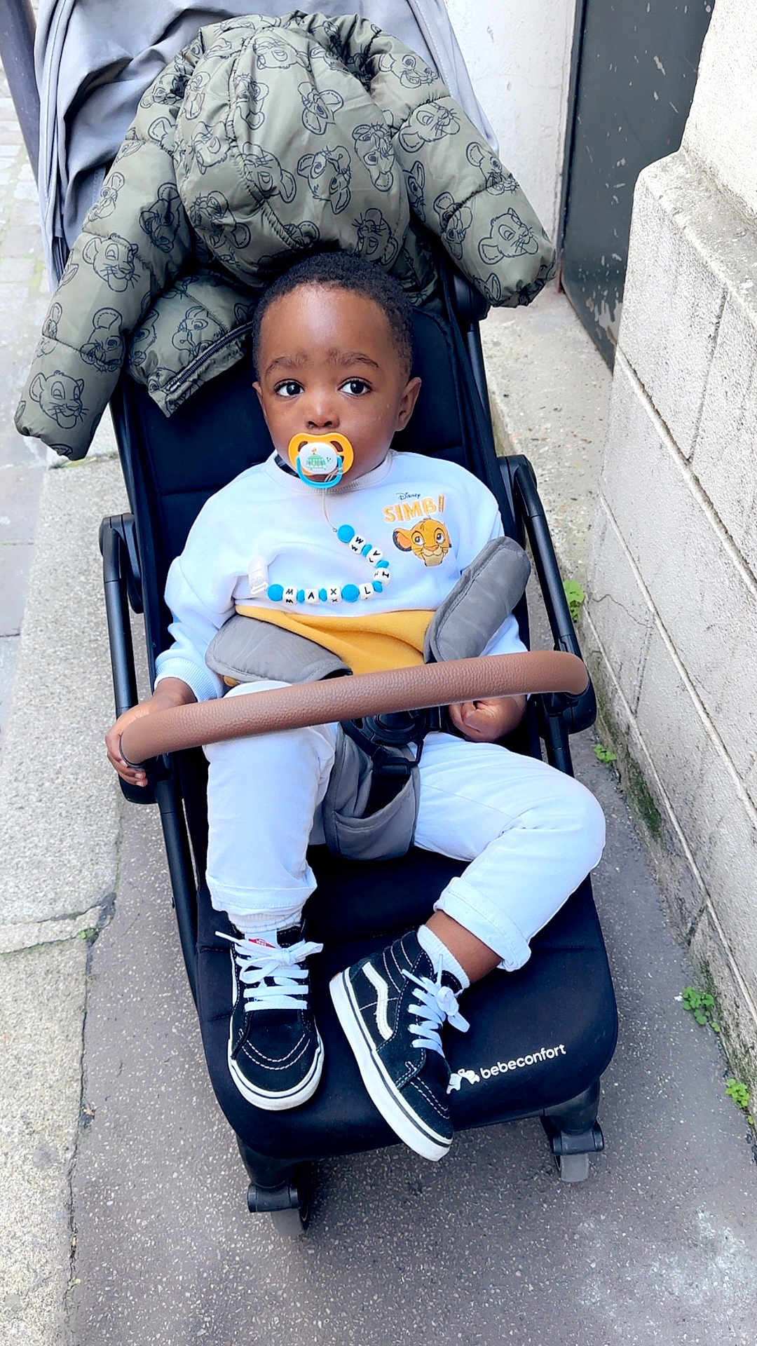 Liam Hugo participe au concours pour gagner de l'argent avec cette photo : child, toddler, stroller, pacifier, sweatshirt, disney, simba, jacket, shoes, sneakers, pants, sidewalk, urban, outdoor, curious, baby, person, clothing, street, daytime