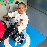 Liam Hugo a rejoint le concours — aidez-le/la à gagner de superbes lots ! toddler, child, tricycle, bus, wheelchair_symbol, blue_floor, jacket, sneakers, smiling, indoor, public_transport, seat, patterned_seat, handrail, window, person, disability_sign, floor_marking, toy, wheel