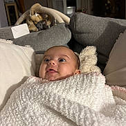 Lou participe au concours pour gagner de l'argent avec cette photo : baby, blanket, cushion, face, indoor, infant, living_room, looking_up, person, portrait, soft_texture, white_blanket, cozy, child, cute, expression, wrapped, seated, home, comfort