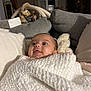 baby, blanket, cushion, face, indoor, infant, living_room, looking_up, person, portrait, soft_texture, white_blanket, cozy, child, cute, expression, wrapped, seated, home, comfort