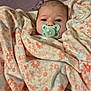 Amelia is registered to the contest to win money with this photo: baby, blanket, pacifier, face, infant, wrapped, sleeping_area, soft_texture, floral_pattern, bed, comfort, child, cute, indoor, resting, warm, person, portrait, young_child, cozy