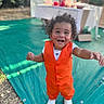 child, toddler, smiling, happy, outdoor, pool, poolside, swimming_pool, party, celebration, orange_outfit, vest, white_shirt, white_shoes, curly_hair, reaching, standing, portrait, summer, backyard